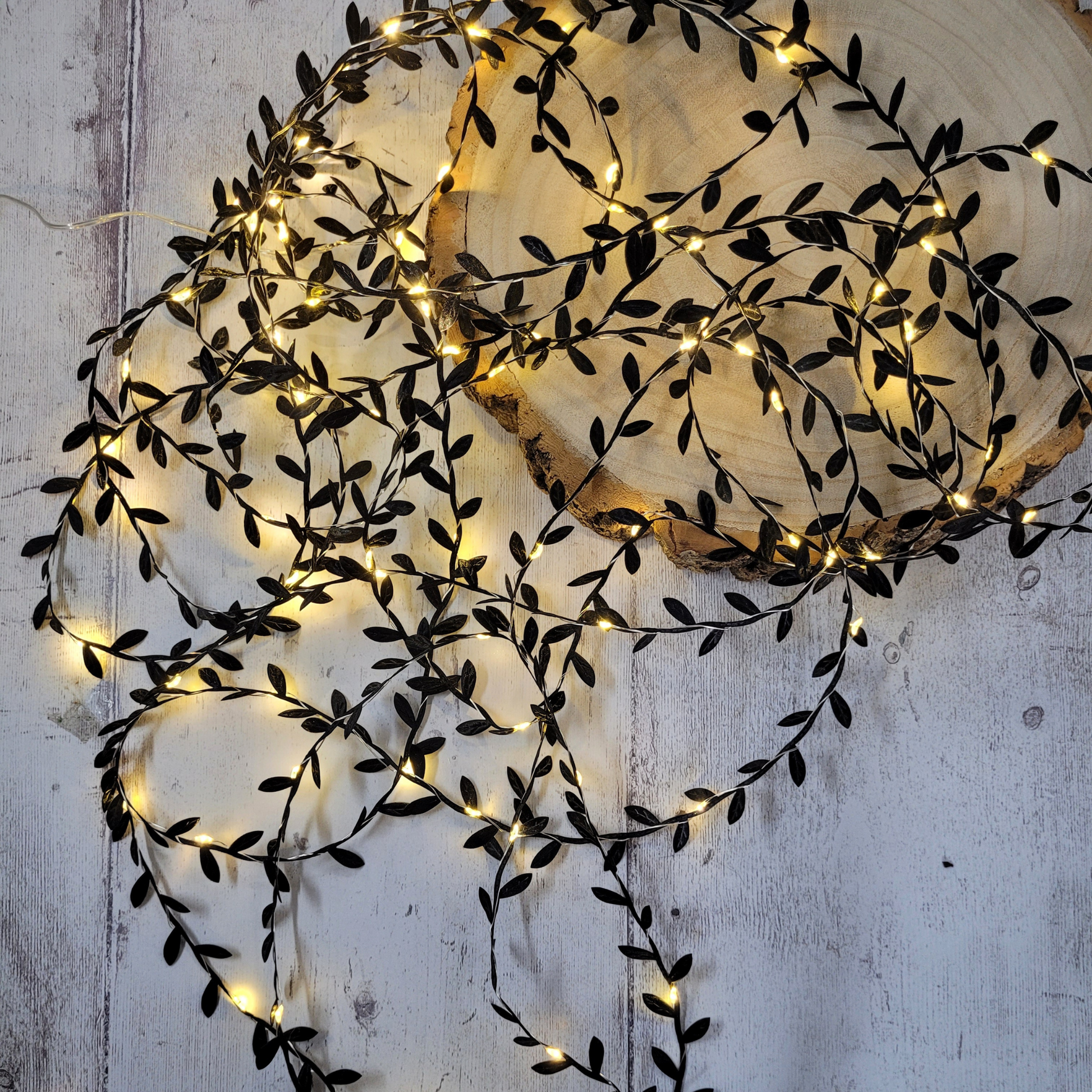 Gothic Black leaf fairy lights draped on a wooden log slice on a grey wooden backdrop
